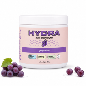 A white plastic tub of Hydra Pure Electrolytes in grape slush flavor, shown on a white background with purple grapes and a green leaf at the bottom left and right.
